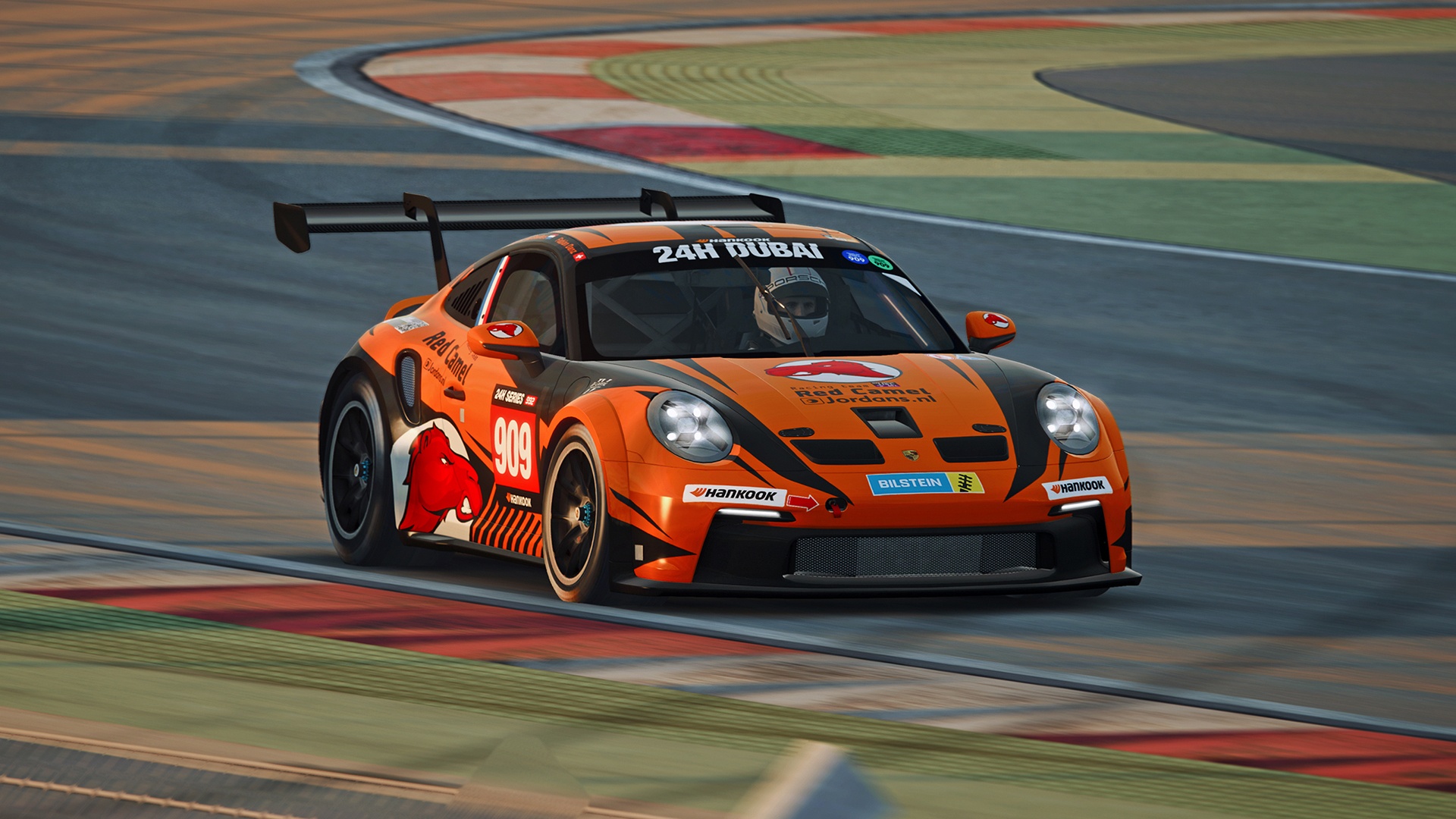 Ein orange-schwarzer Rennwagen mit der Nummer 999 und einer Red-Bull-Grafik an der Seite rast während der 24 Stunden von Dubai um eine Kurve auf einer Rennstrecke.